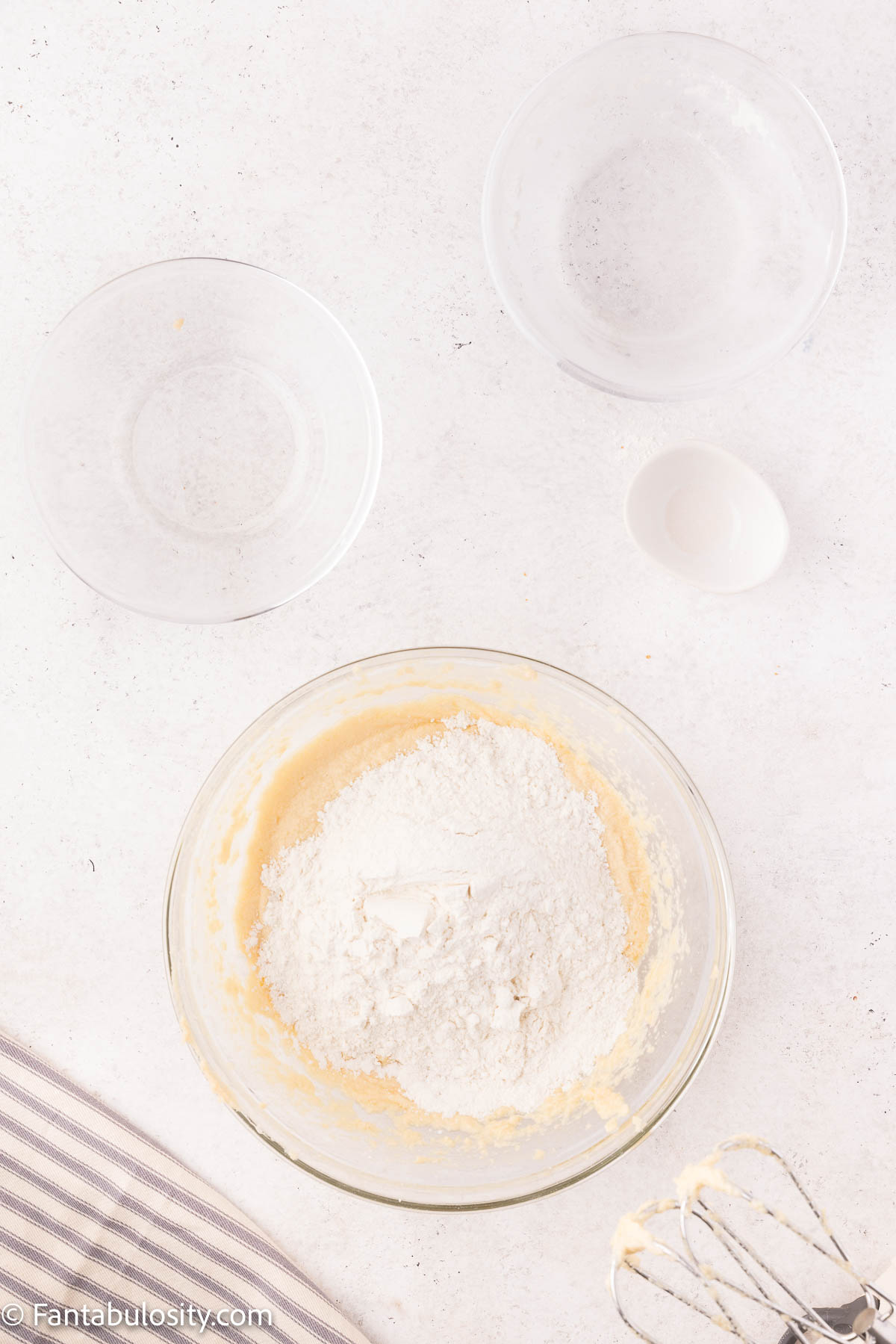 Flour and baking soda have been added to a mixing bowl with cupcake batter in it