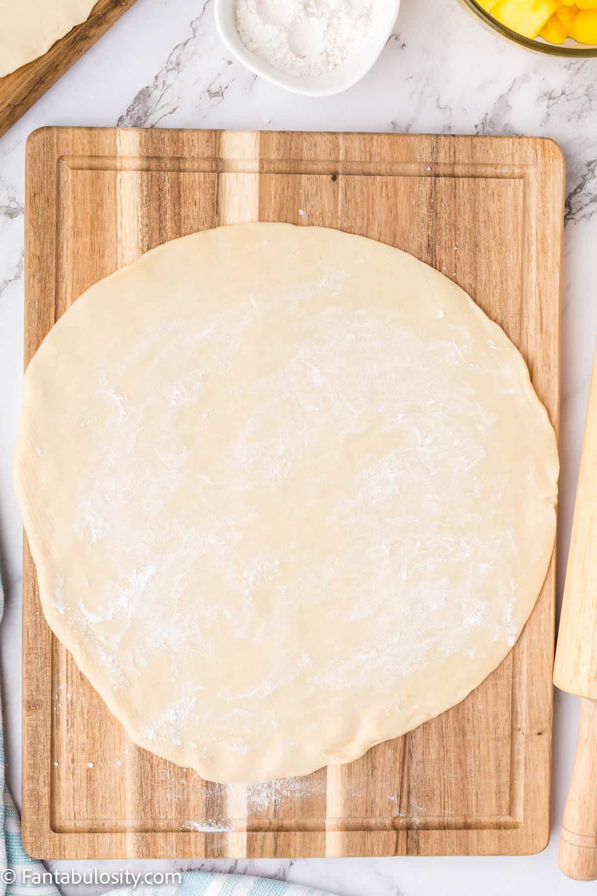 A piece of pie dough rolled out on a cutting board with flour sprinkled over it. 