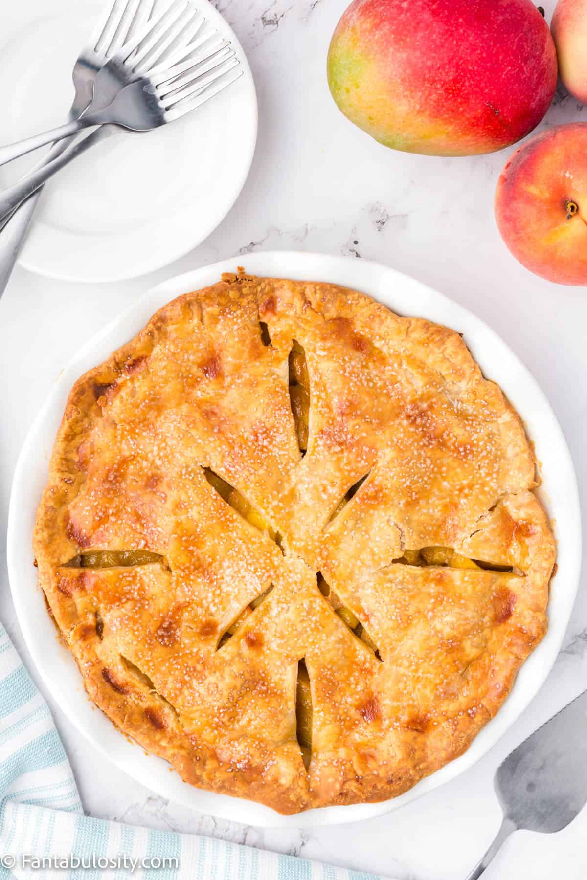 A fully baked peach mango pie sitting on a counter with a nice golden brown crust.