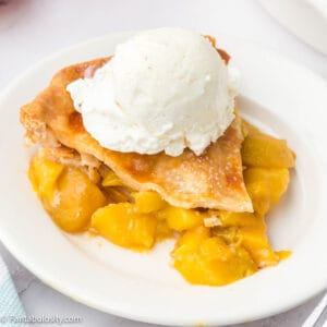 A slice of peach mango pie on a white plate topped with a scoop of vanilla ice cream.