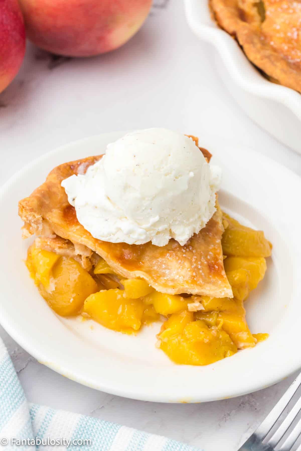 A slice of peach mango pie on a white plate, topped with a scoop of vanilla ice cream. 