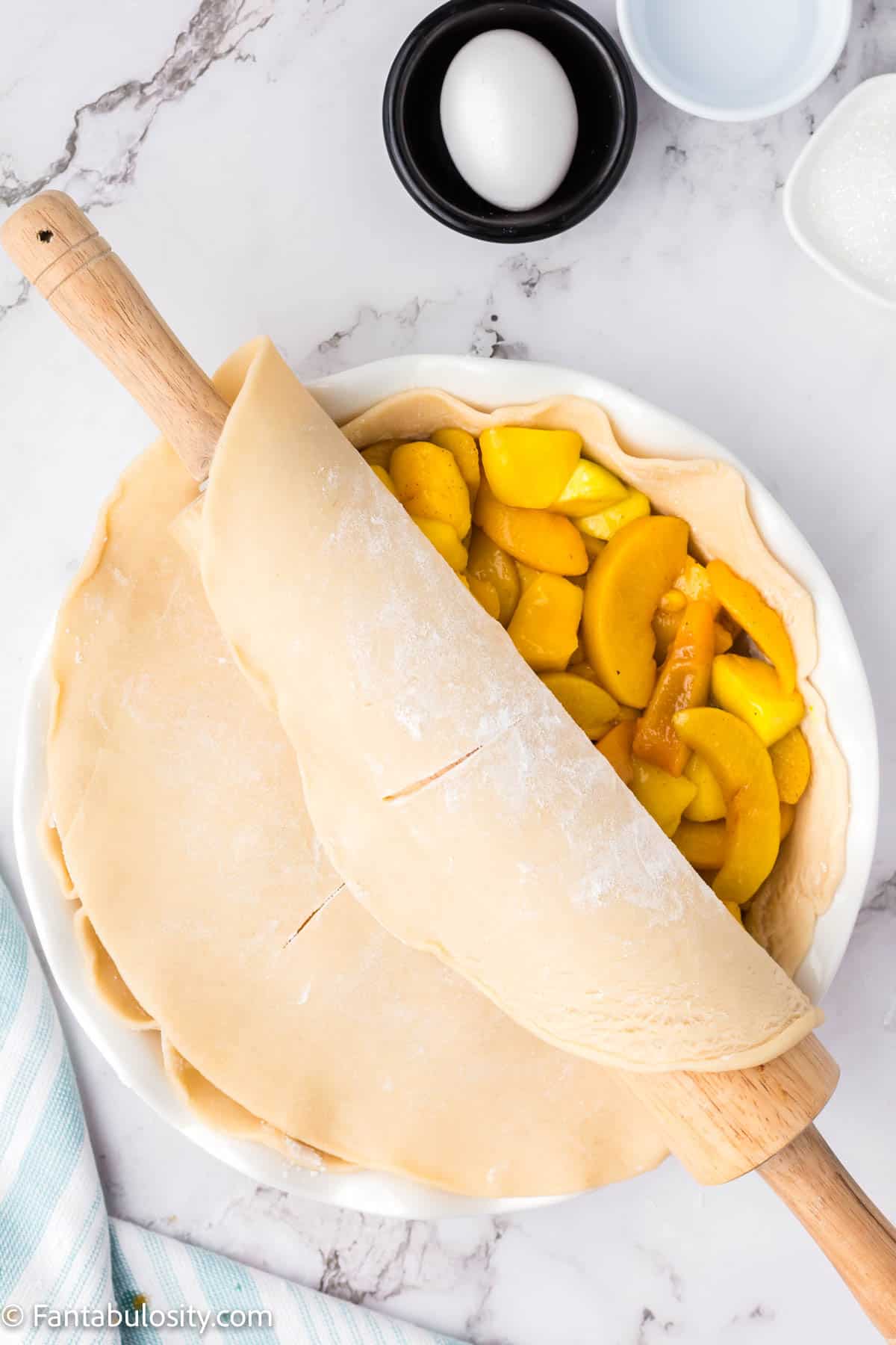 A top pie crust being placed onto a peach mango pie.
