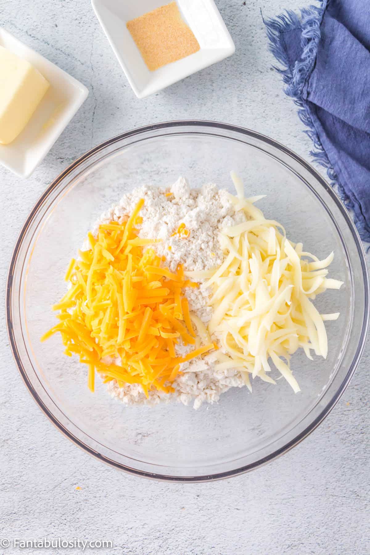 Bisquick mix, shredded cheddar cheese, and shredded mozarella cheese in a glass bowl.