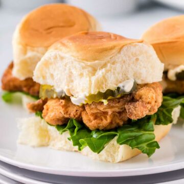 Fried chicken sliders on white plate, topped with mayo, lettuce and pickles.
