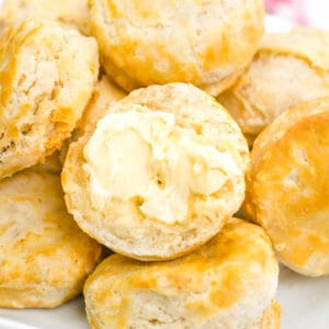 Cooked, air fried frozen biscuits on white plate, with one biscuit with butter on top.