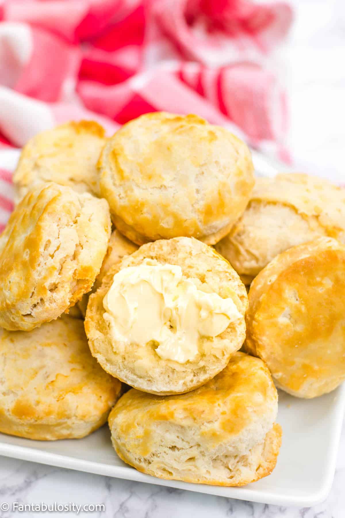 Stack of biscuits with one biscuit in the front, sliced with butter.