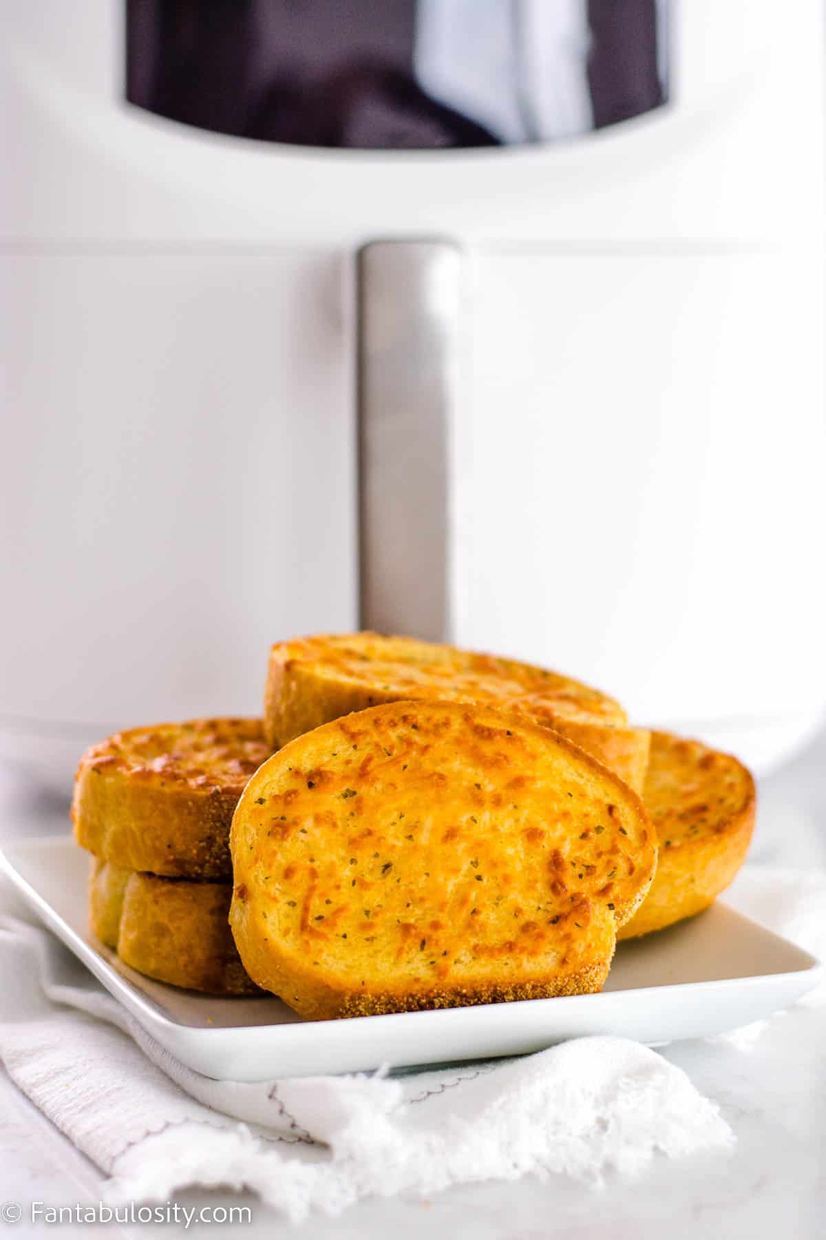 Cooked frozen garlic bread, sitting on white plate in front of an air fryer.