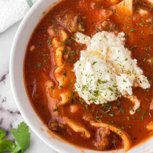 Lasagna soup in white bowl with dollop of ricotta cheese on top.