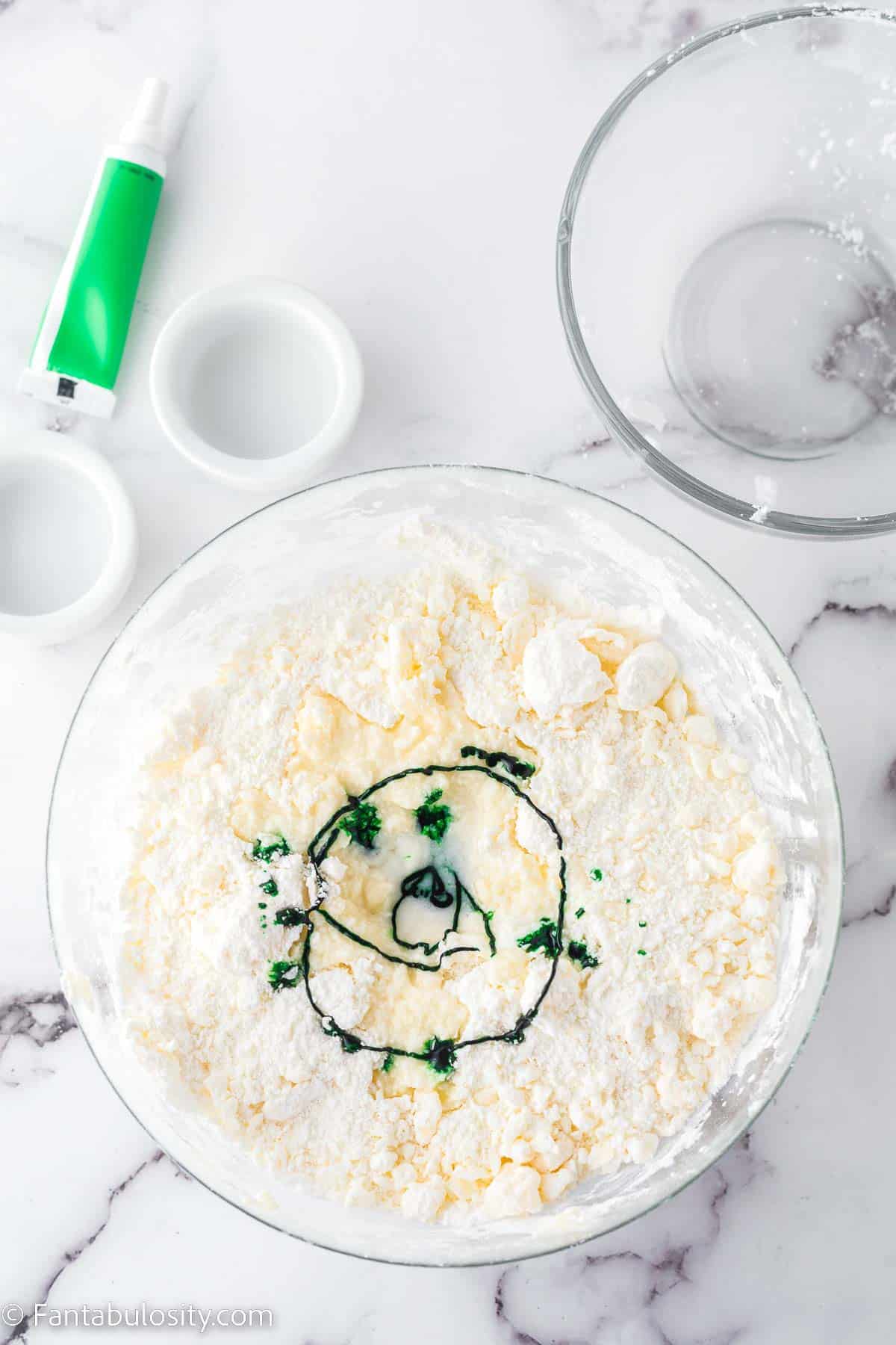 Green gel food coloring added to butter and sugar, in glass bowl.