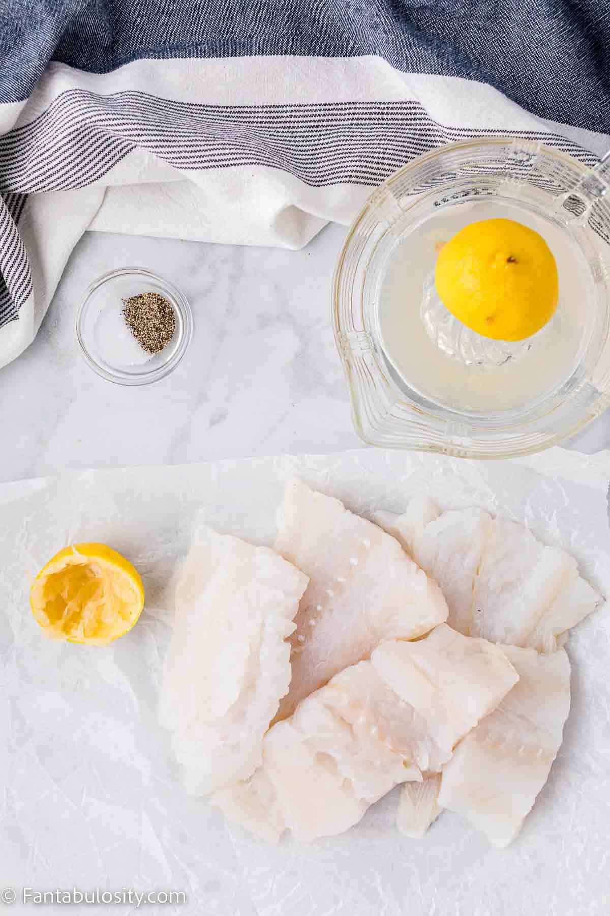 Uncooked cod filets sitting on cloth, next to lemon.