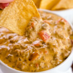 Rotel dip with meat, in white bowl, that has a chip dipping in to it.