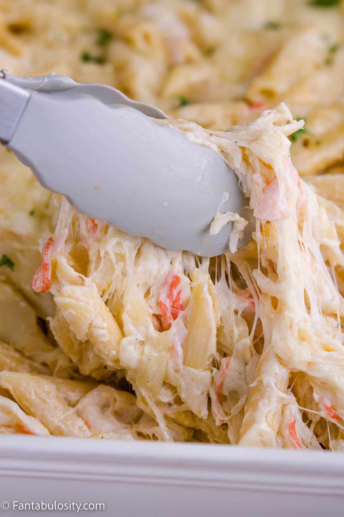 Crab pasta bake being pulled up out of dish with tongs.