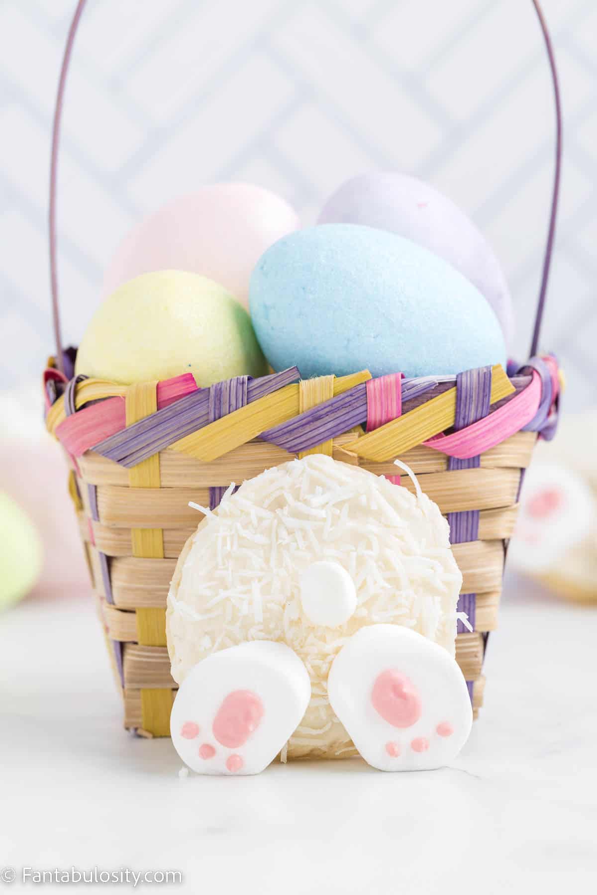Bunny Butt Cookie leaned up against Easter basket that has eggs in it.
