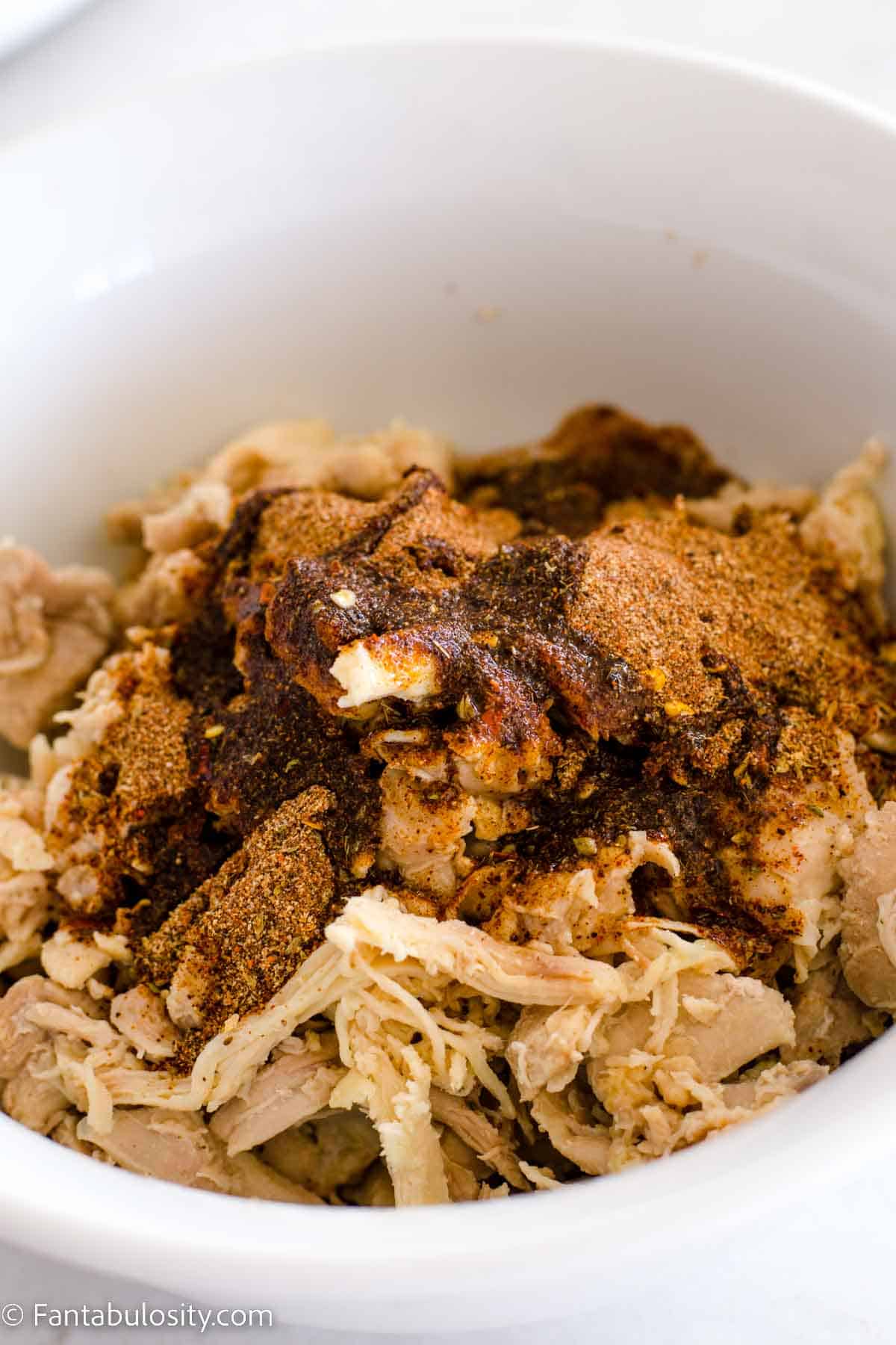Shredded Chicken with taco seasoning, lime juice and oil in bowl.
