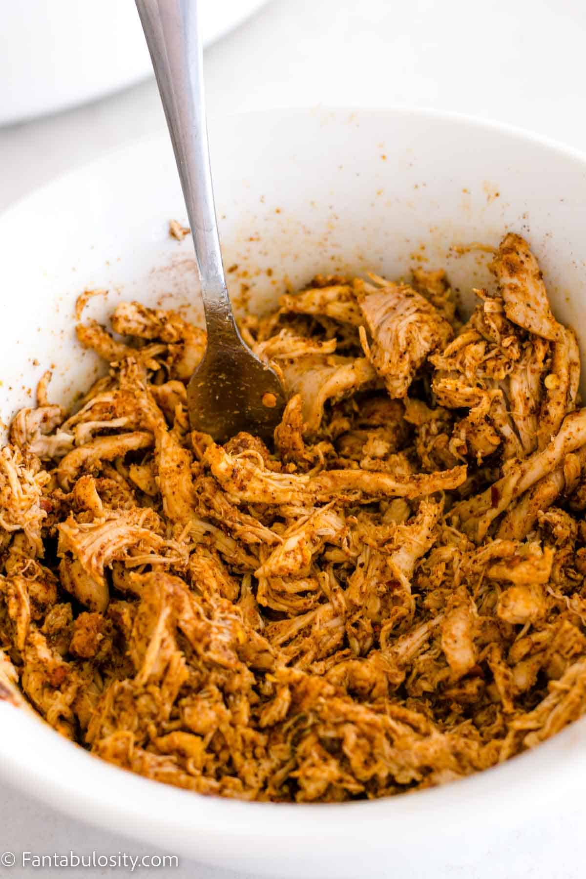 Cooked shredded chicken in bowl with taco seasoning, lime juice and oil.