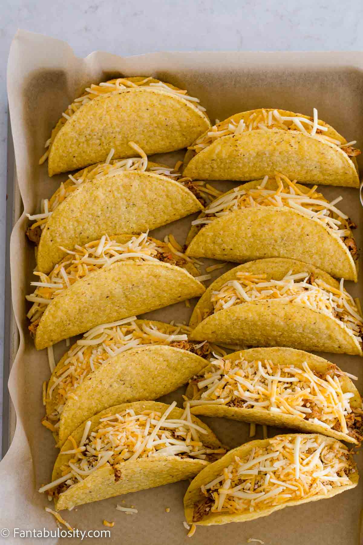 Crispy taco shells on baking sheet, filled with chicken and cheese.