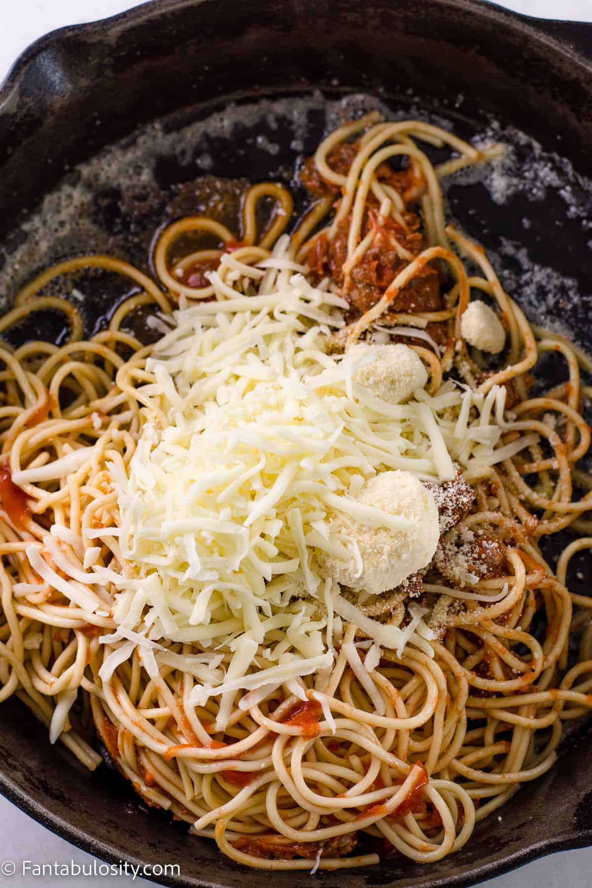 Some of the mozzarella and parmesan cheese sprinkled on top of leftover spaghetti in cast iron.