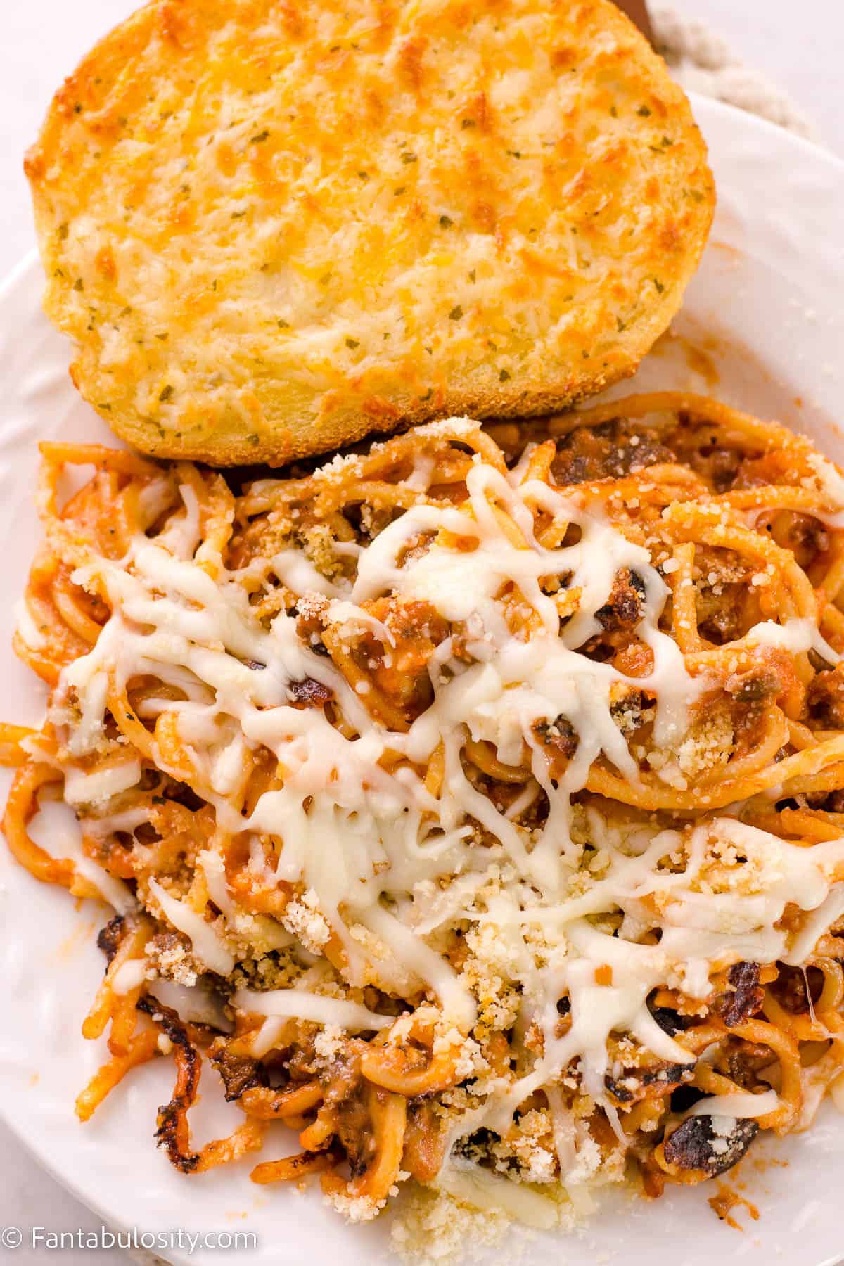 Fried spaghetti on white plate next to garlic Texas toast.