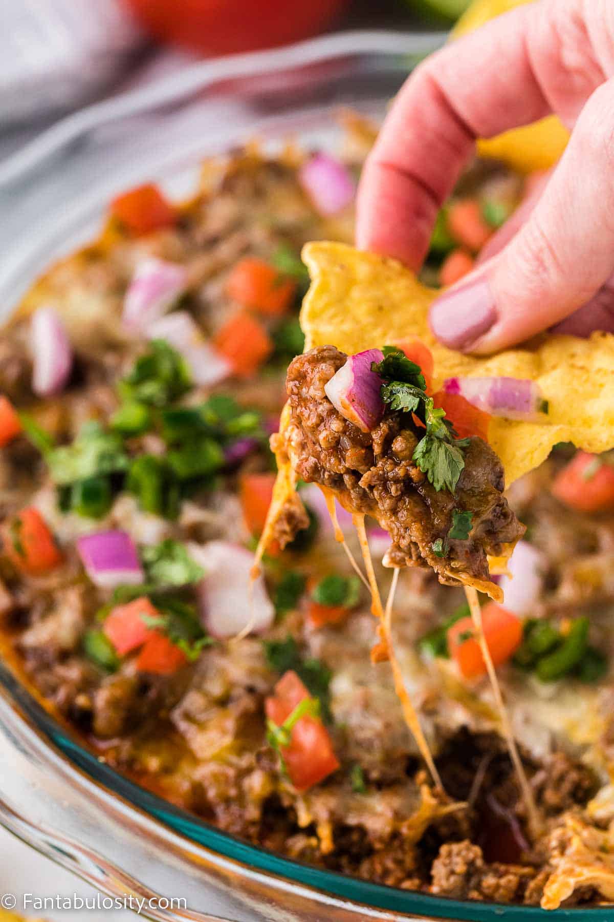 Hot taco dip being lifted out of baking dish with a chip.