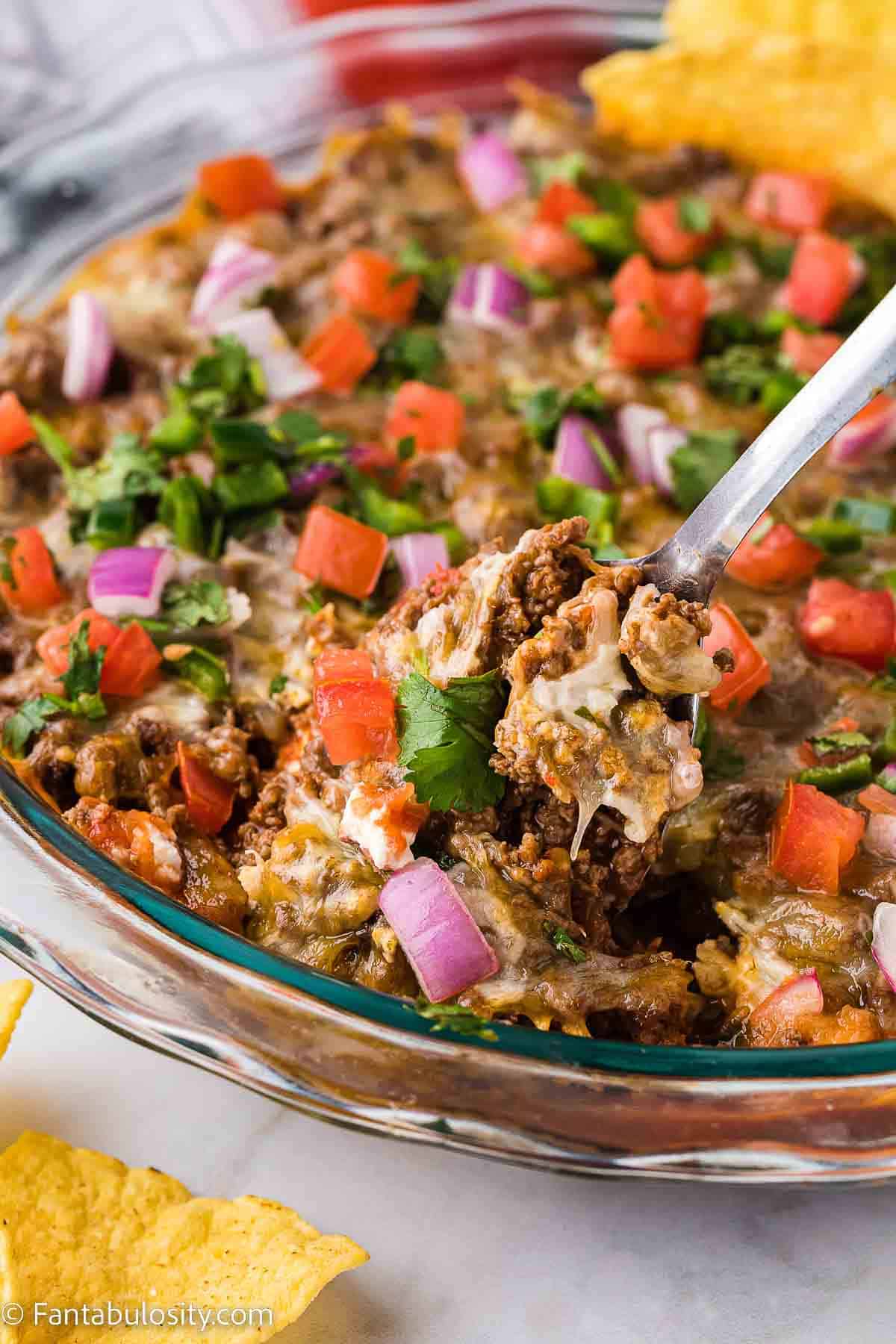 Hot taco dip in a pie plate with a spoon dishing out a serving.