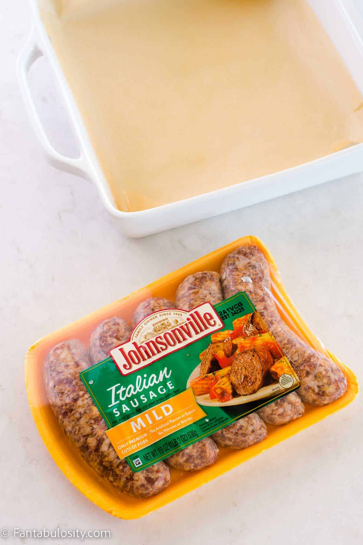 Uncooked Italian sausages in packaging, on white counter.