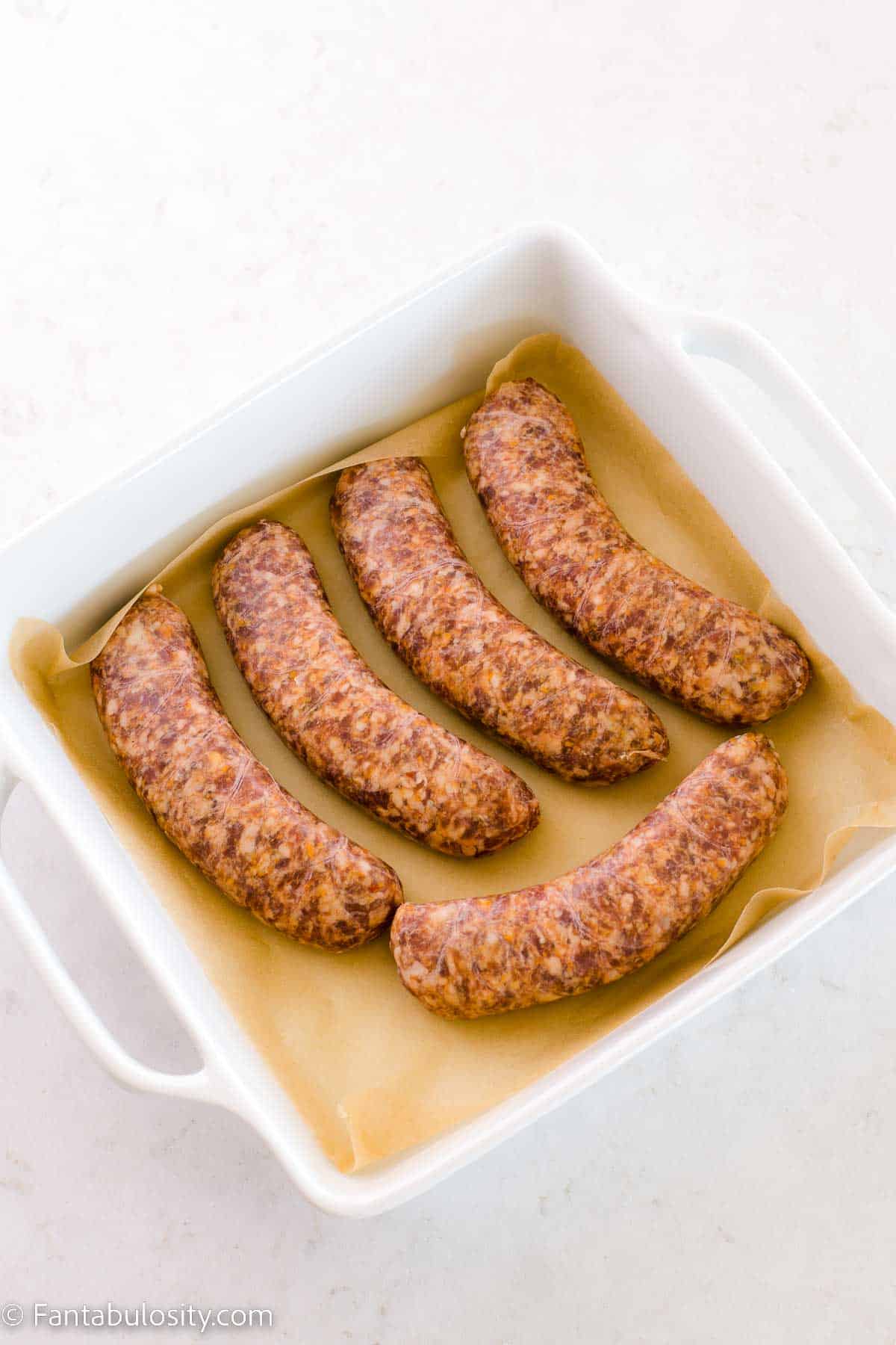 Uncooked sausages in baking dish on top of parchment paper.