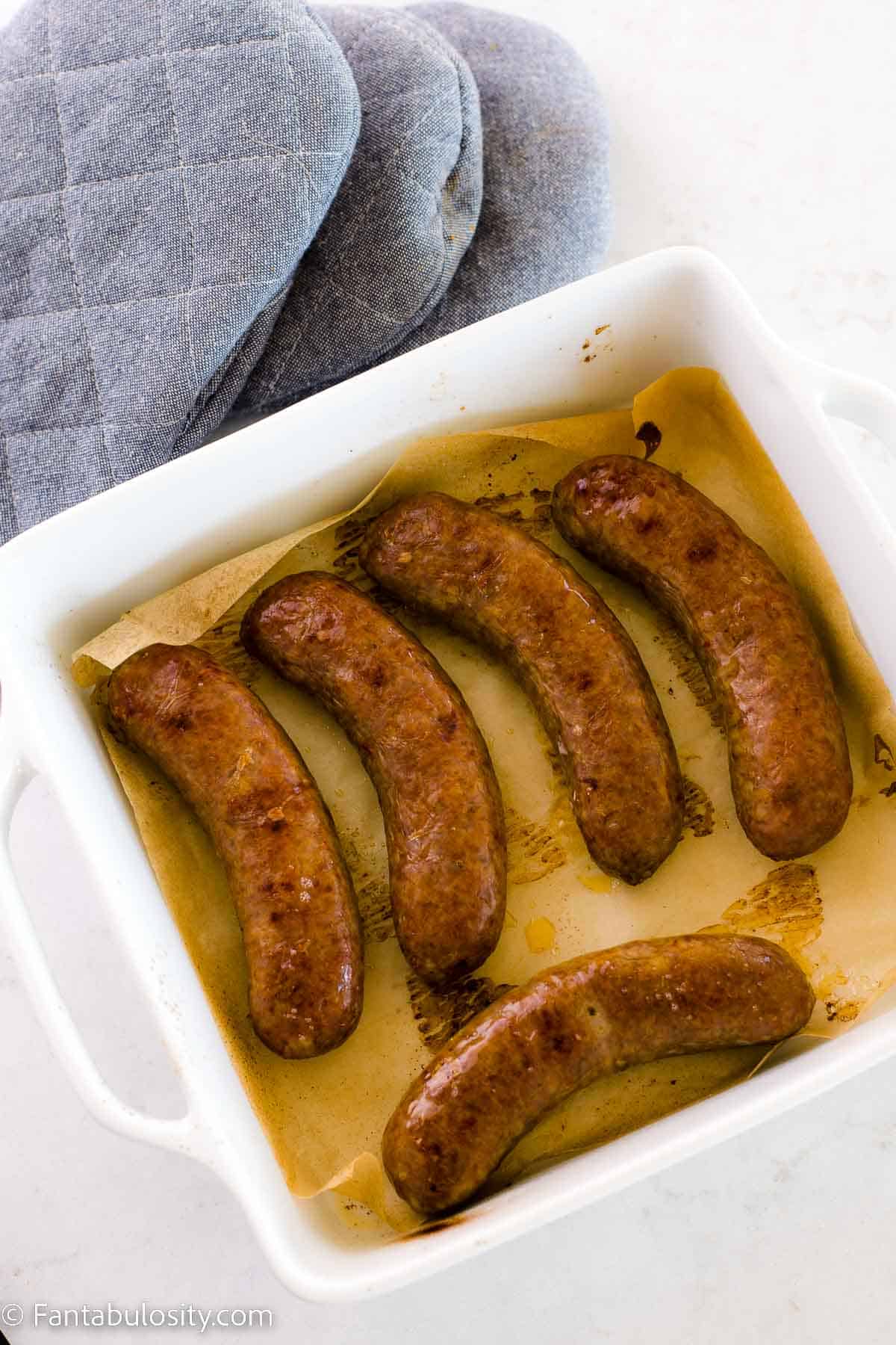 Cooked Italian sausages in baking dish on white counter.