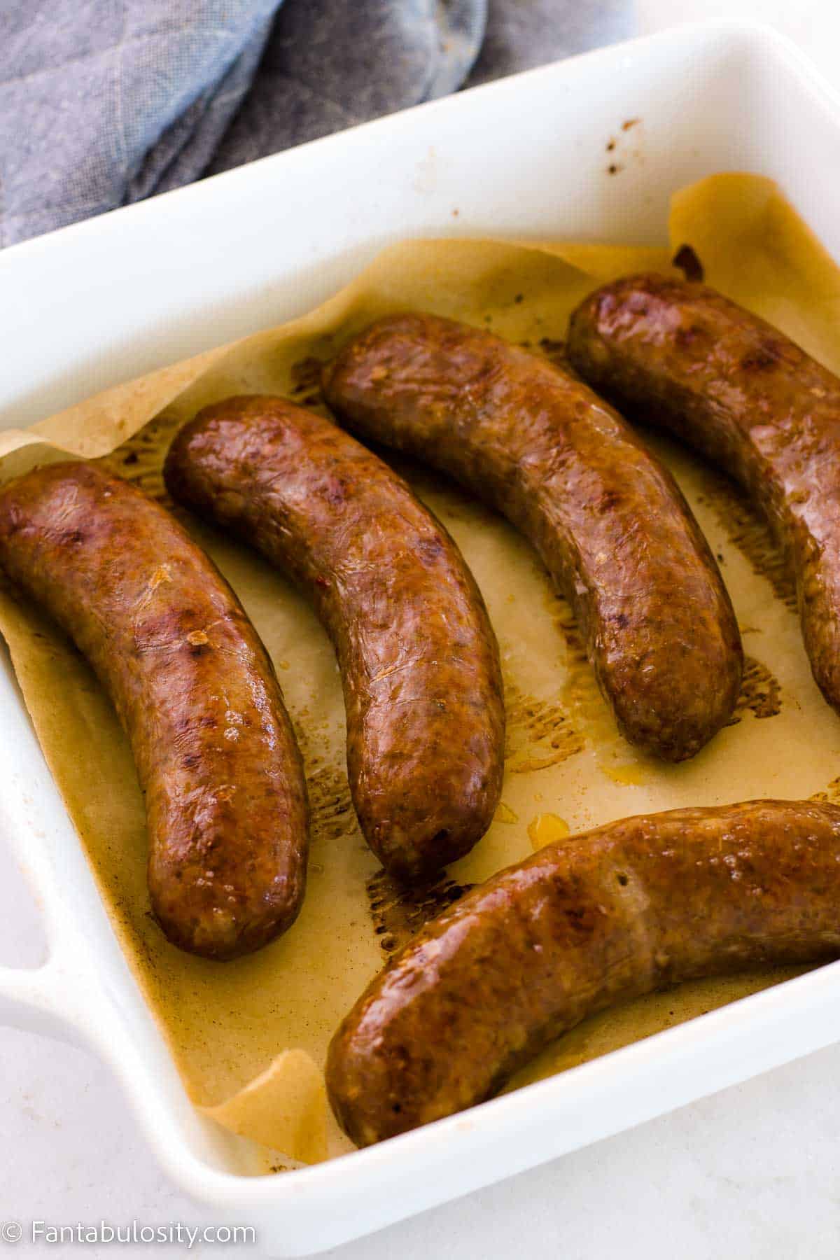 Oven cooked sausages in baking pan with parchment paper.