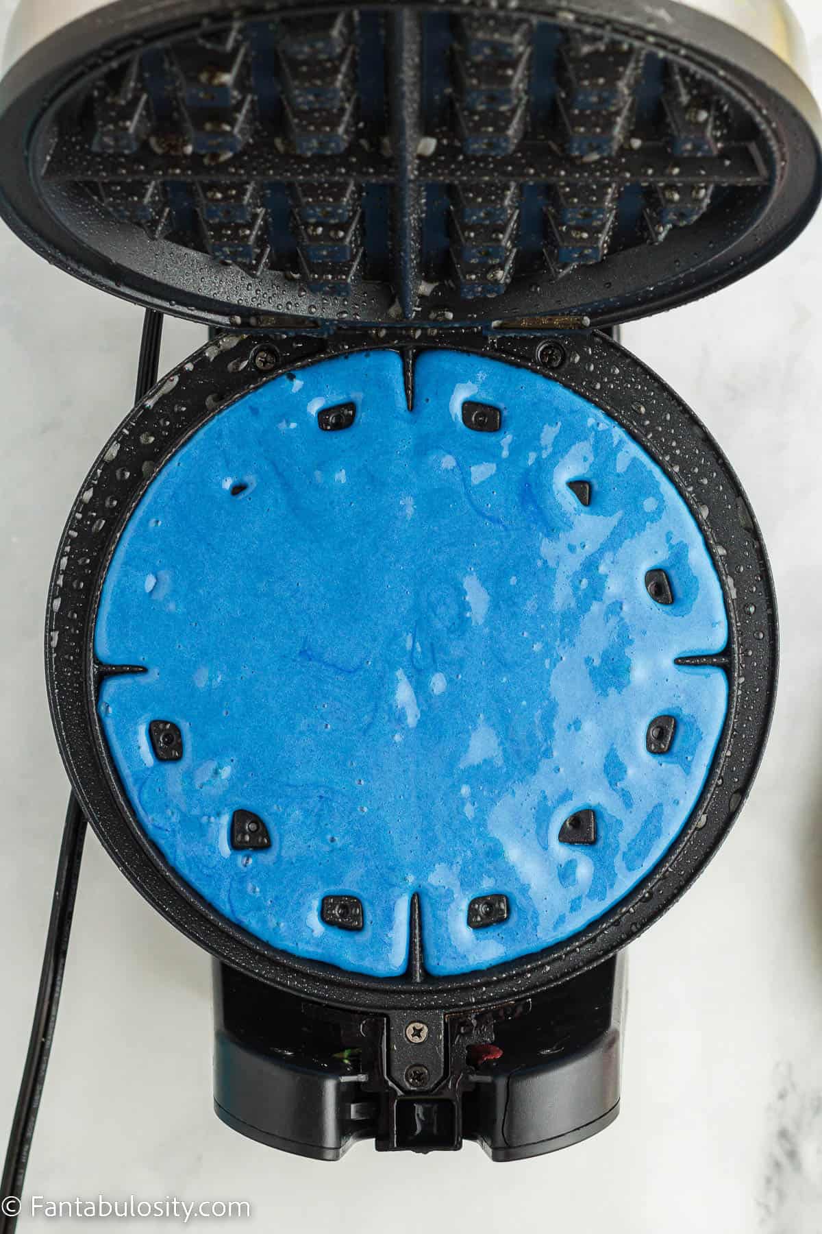 Blue waffle batter in waffle iron.