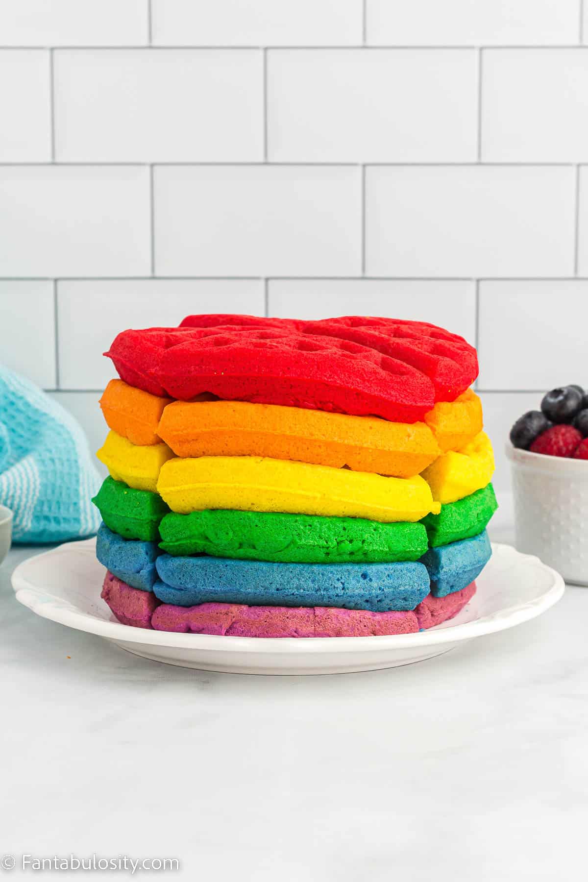 Stack of rainbow waffles on white plate.