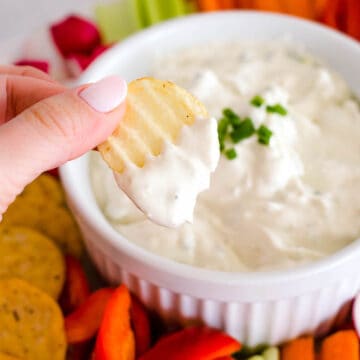 Blue cheese dip in small white bowl, with hand holding chip.