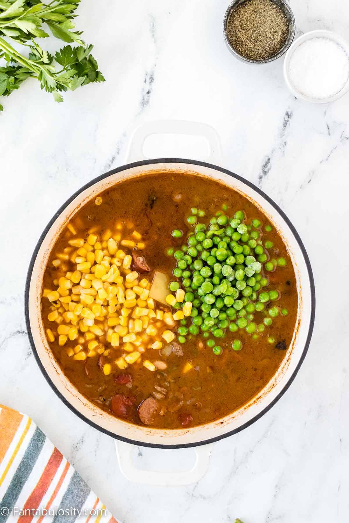 Frozen corn and peas added to cowboy stew in dutch oven.