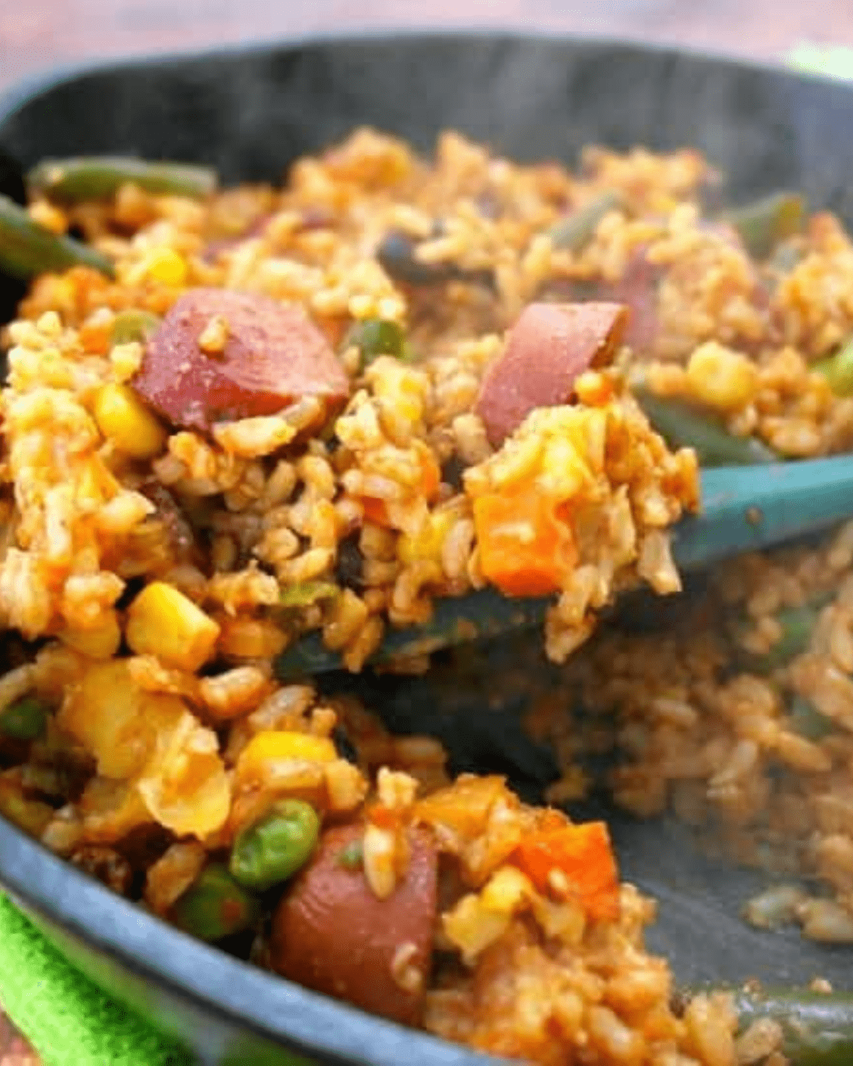 Smoked sausage, rice and veggies in a skillet with a spoon