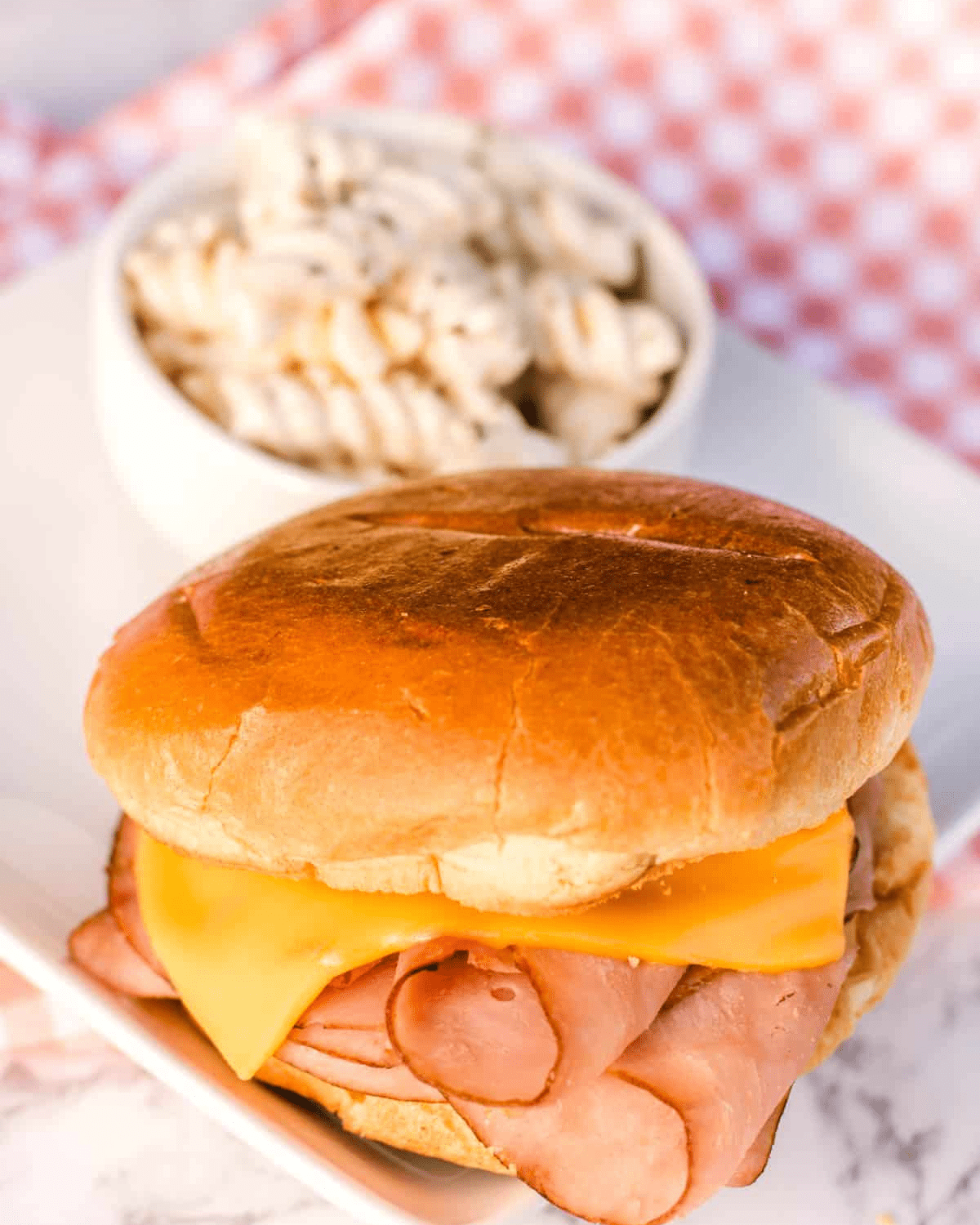 ham and cheese on a bun with pasta in a bowl