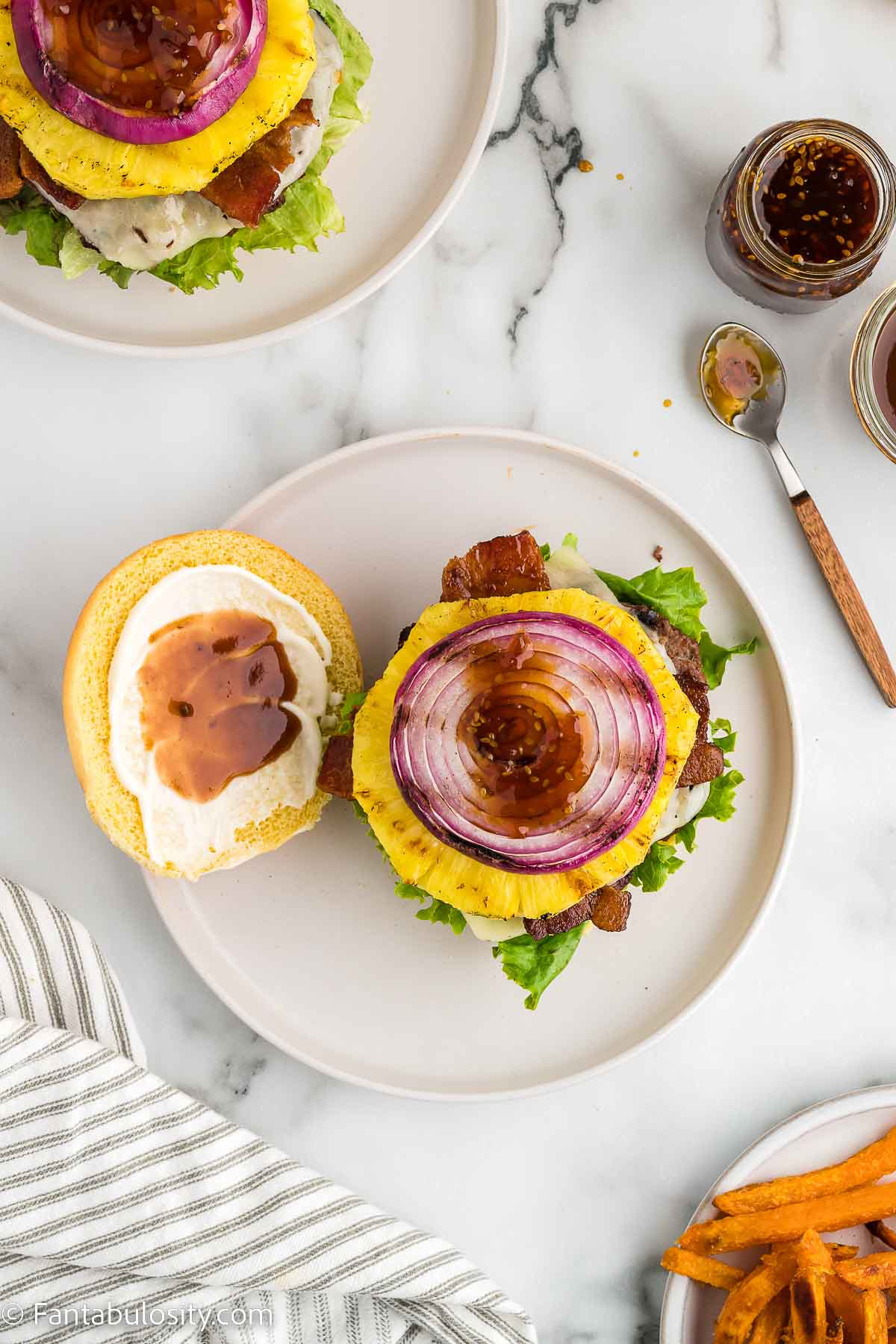 Building an aloha burger with all of the toppings on a white plate and white counter.