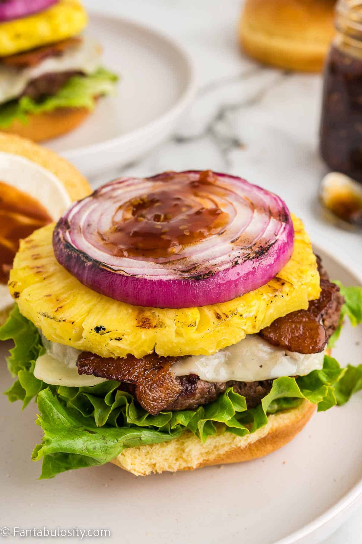 Red onion, teriyaki sauce, bacon, lettuce and cheese on burger.