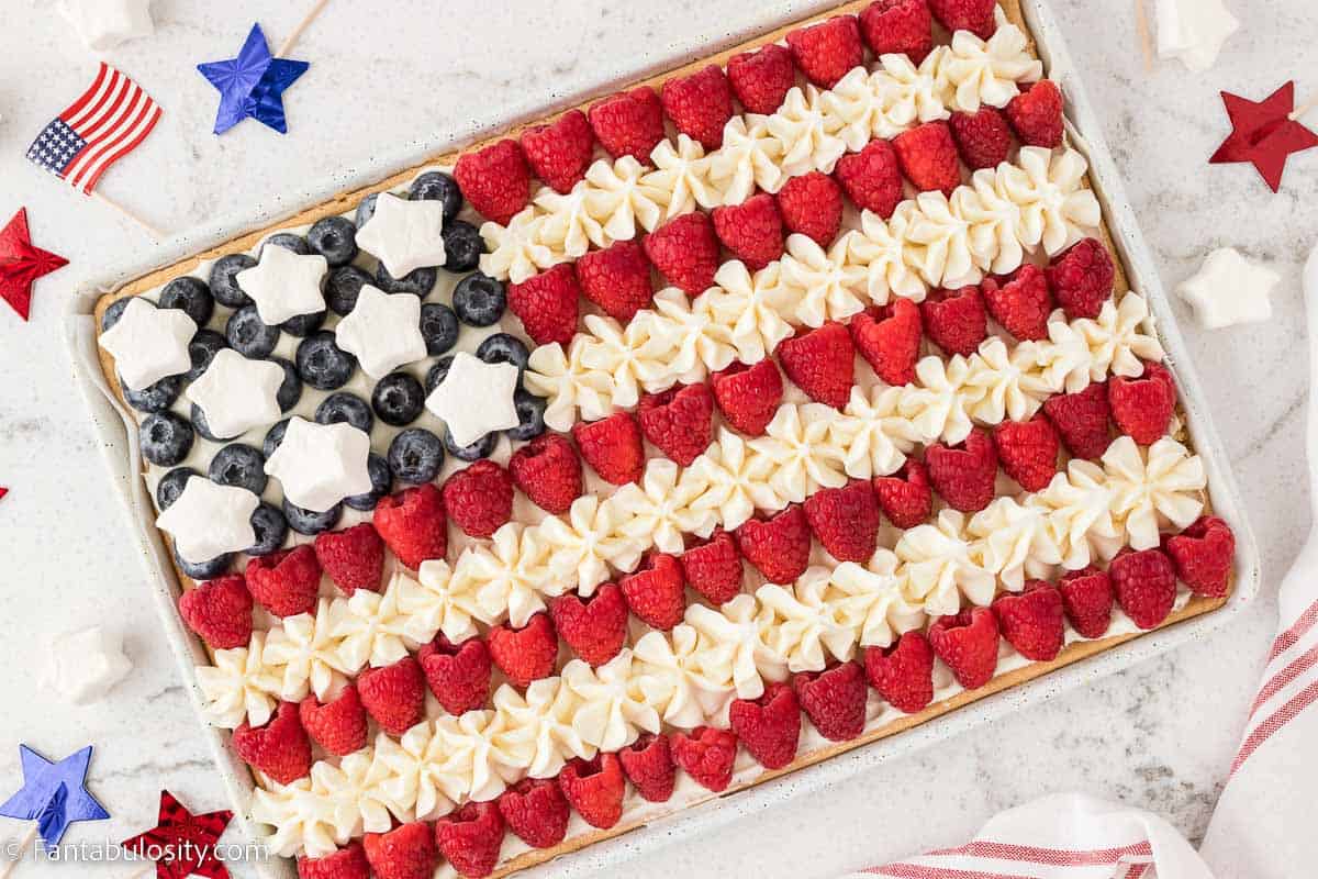 American flag fruit pizza on marble counter with red, white and blue stars surrounding it.