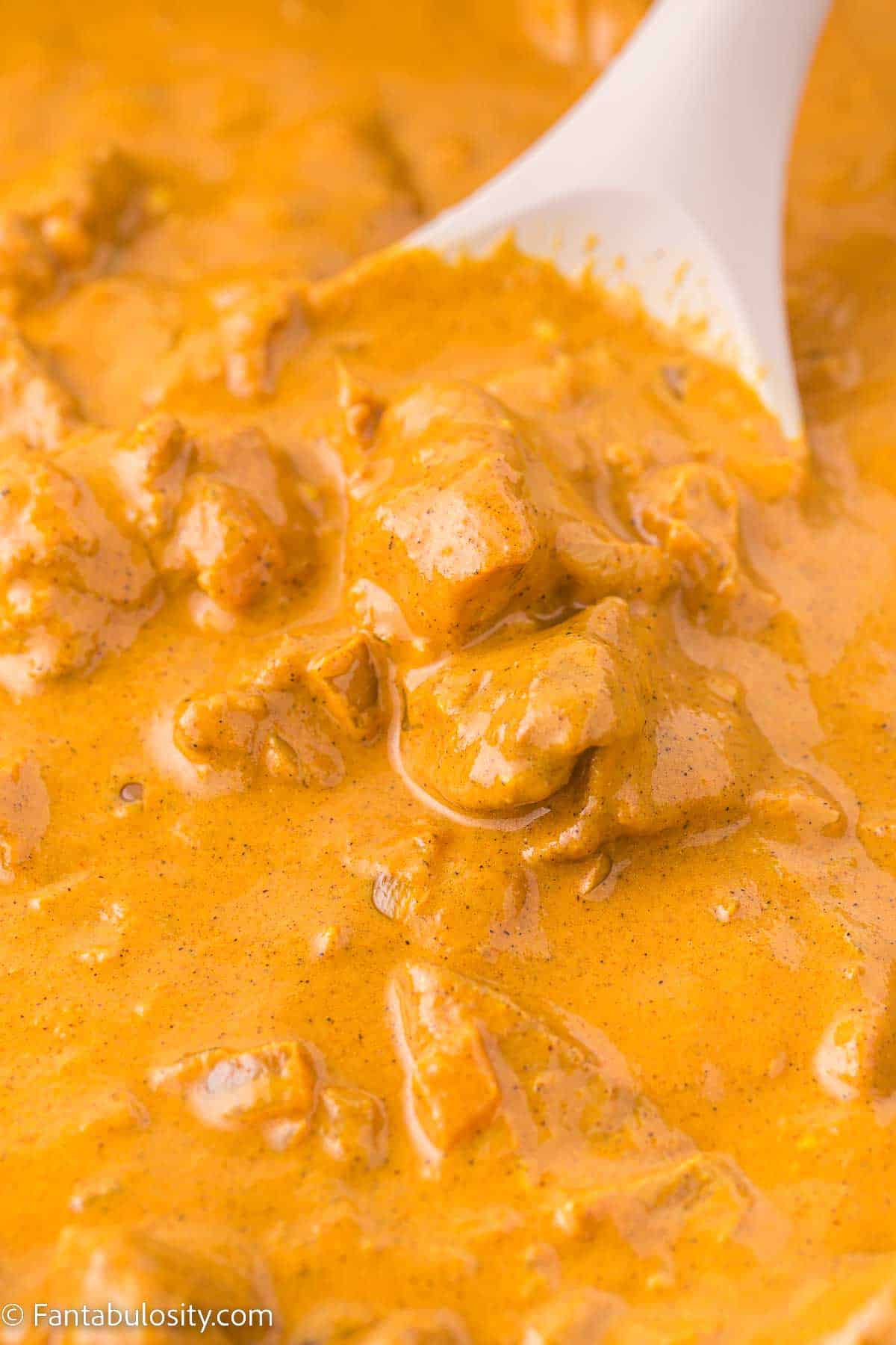 Close up of butter chicken in skillet, with serving spoon dipped in.