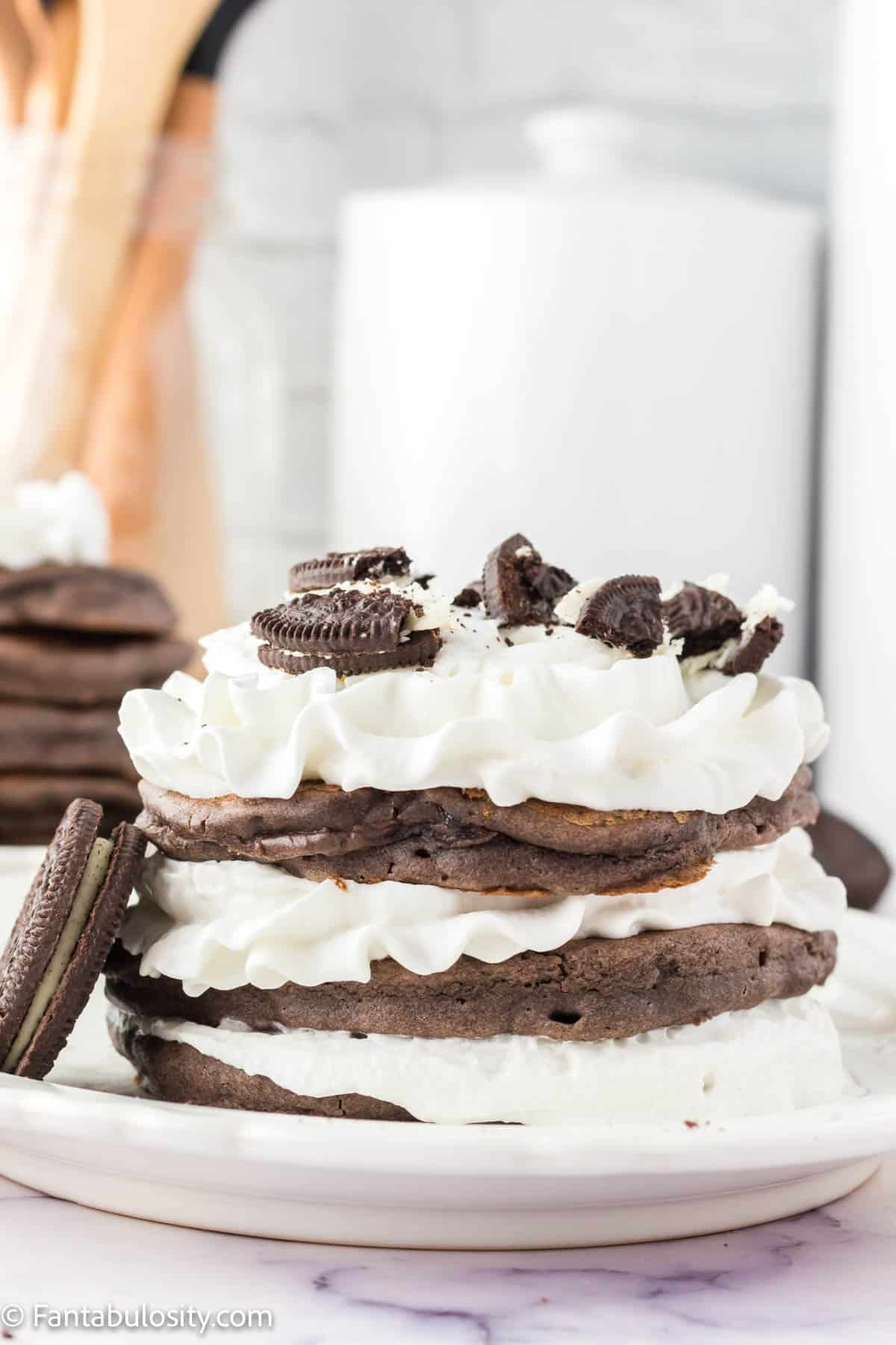Stacked Oreo pancakes on white plate, with Oreo leaning up against stack.