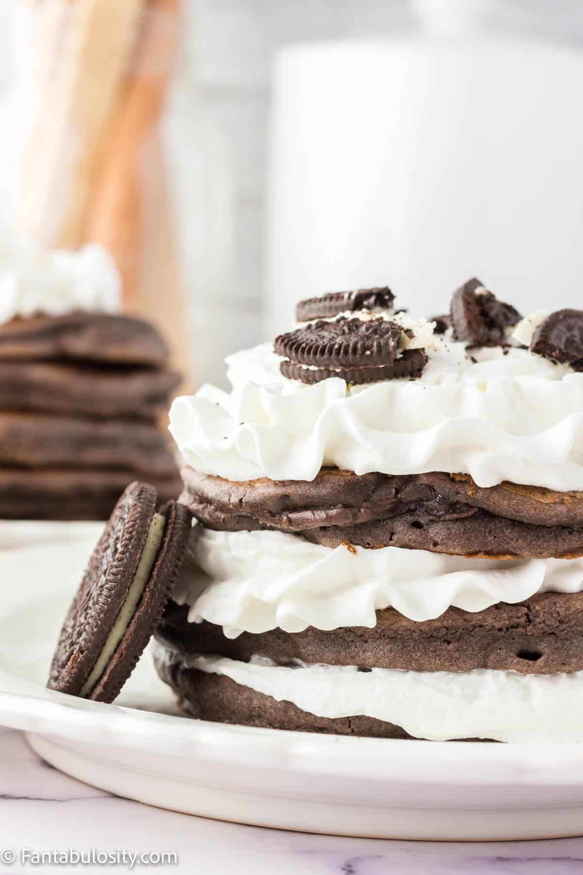 Stacked Oreo pancakes with whipped cream and an Oreo cookie leaning next to them.