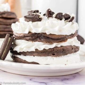 Stacked Oreo pancakes on white plate, topped with whipped cream.