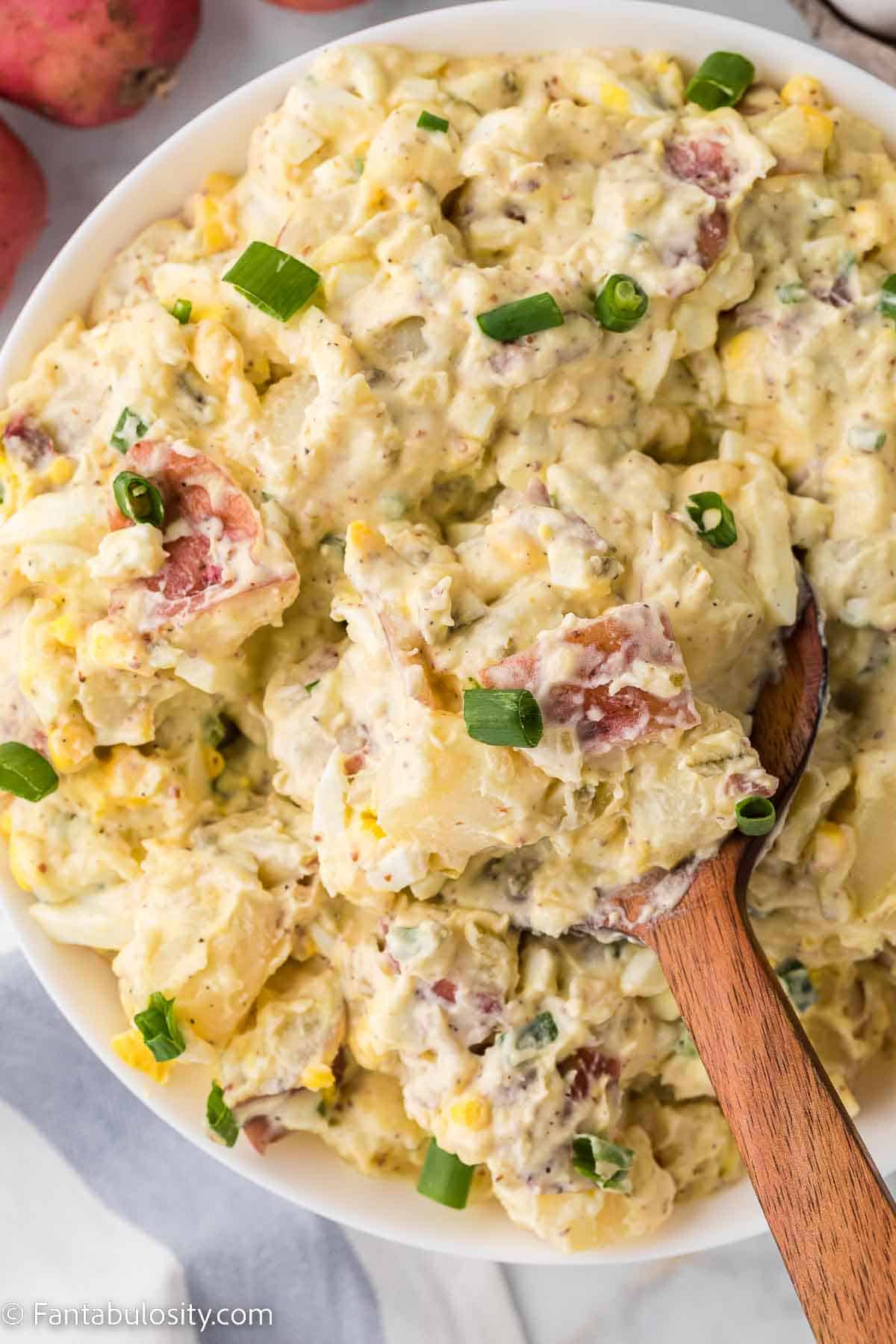 Red skin potato salad in large white serving bowl with wooden spoon.
