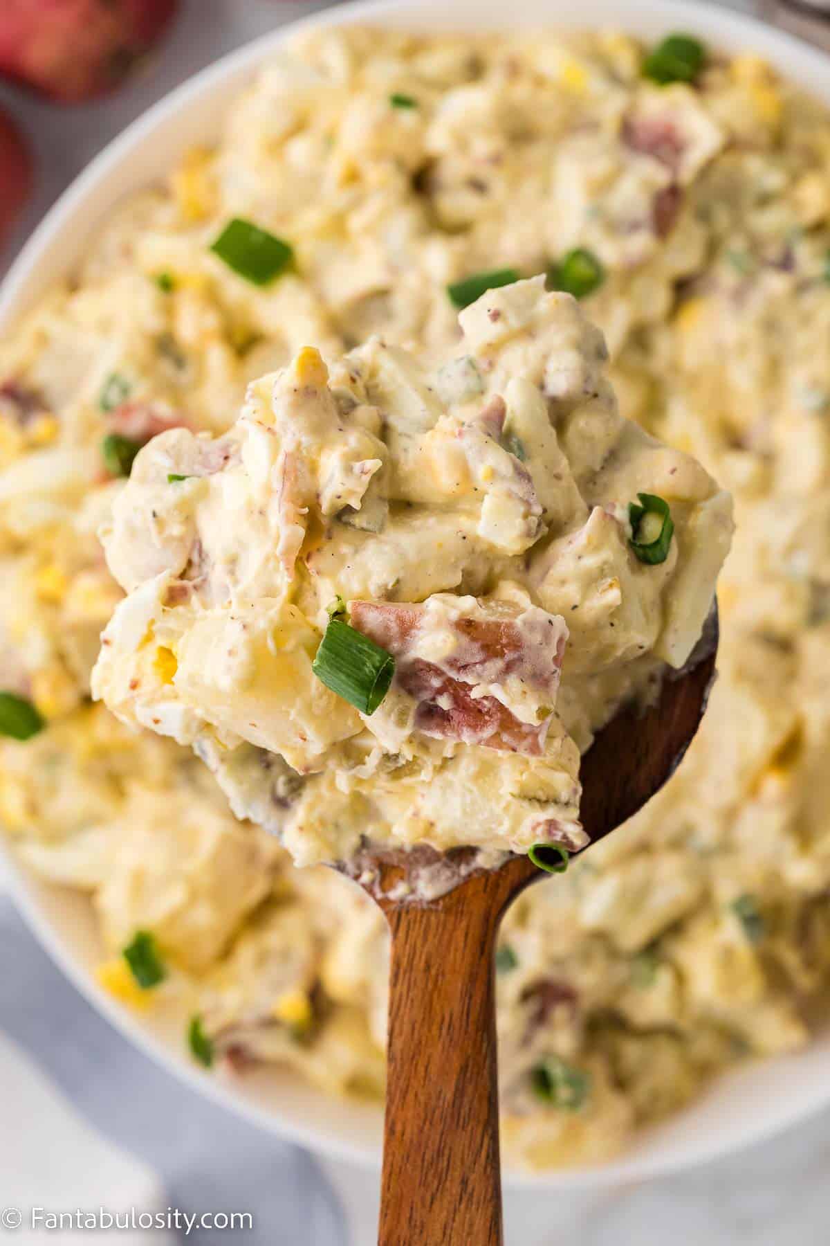 Wooden spoon holding serving of red skin potato salad.