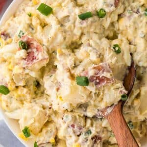 Close up of red skin potato salad in white bowl, with wooden spoon.