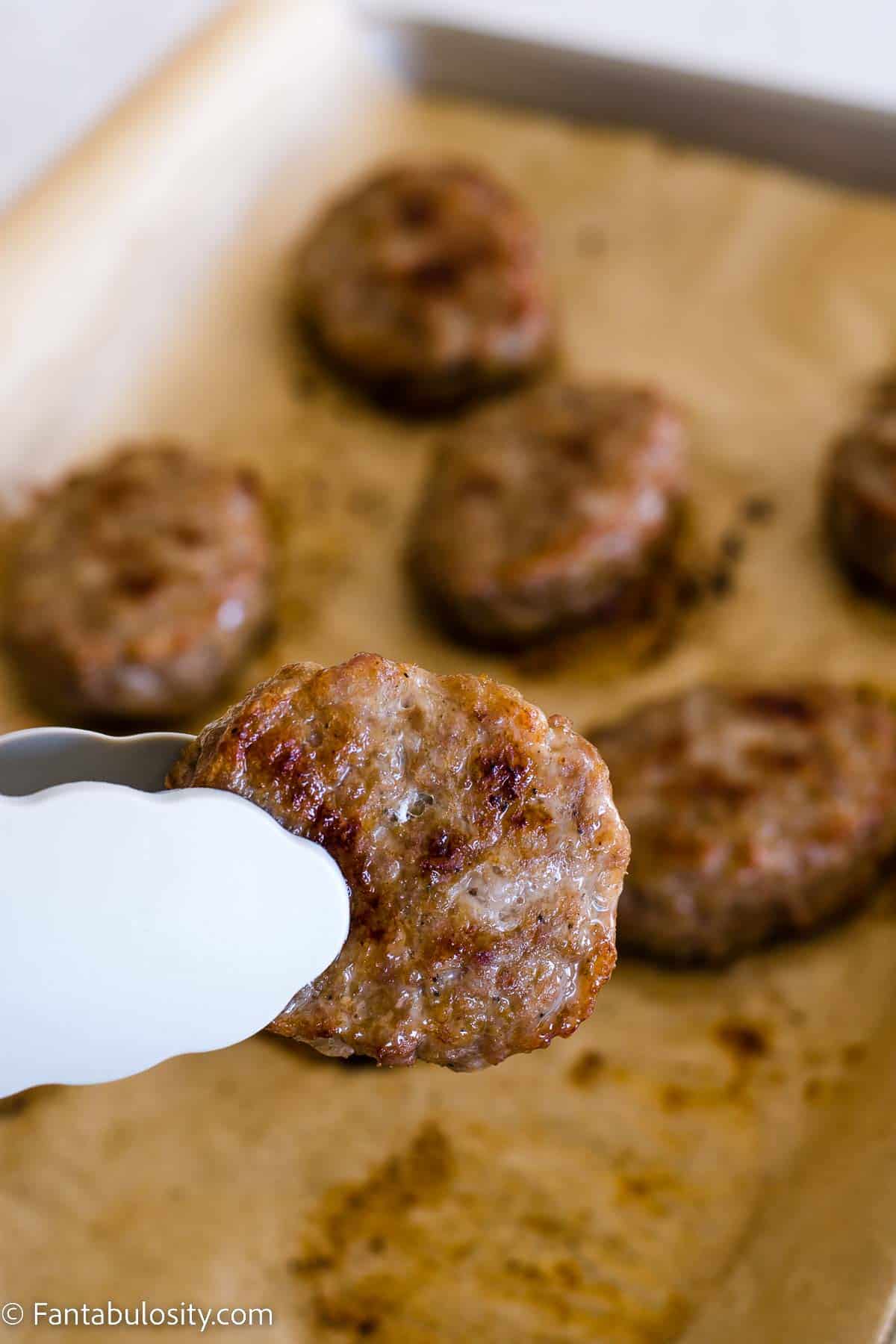 Baked sausage patty being held by tongs.