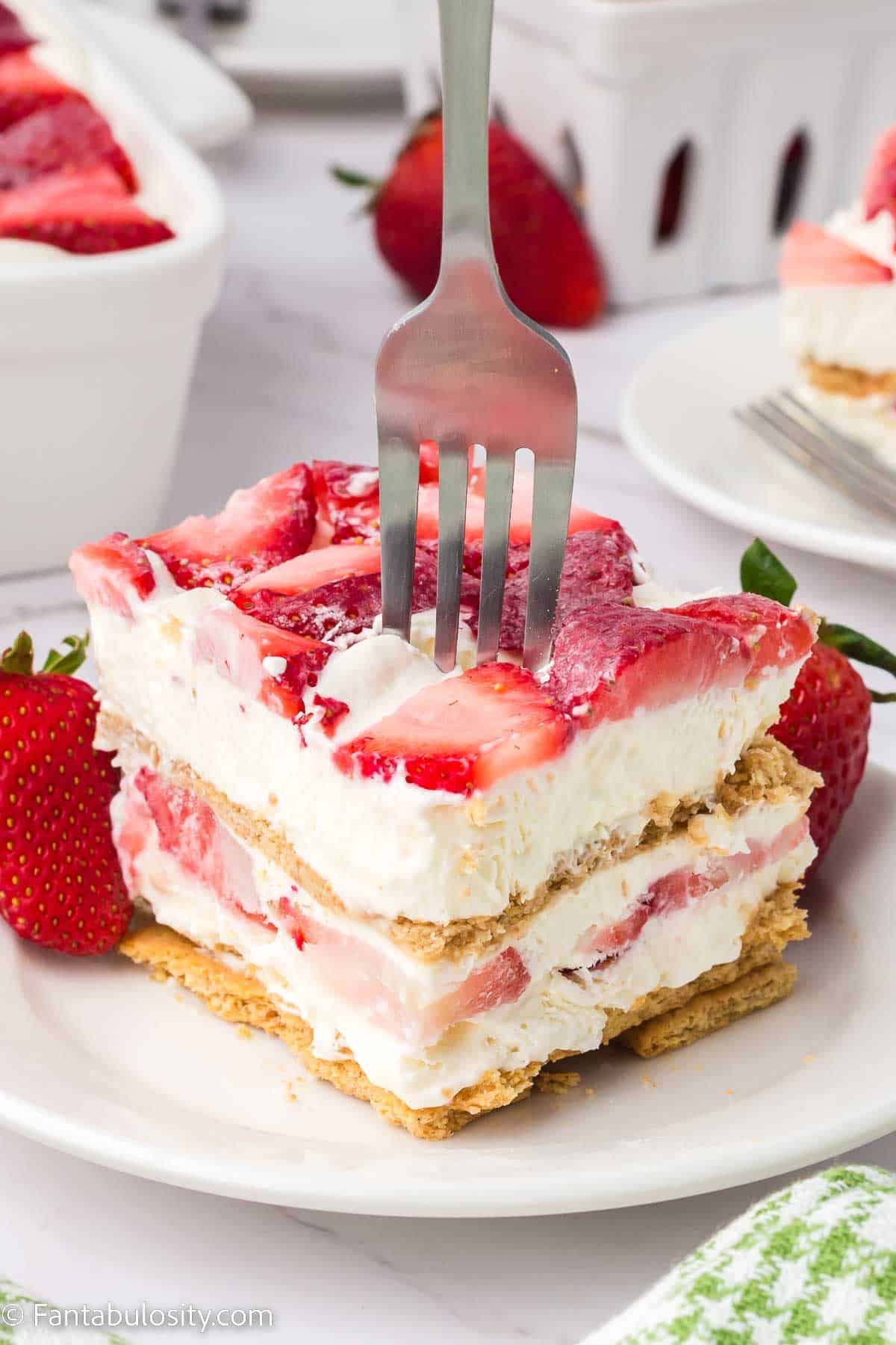 Strawberry cream cheese icebox cake on white plate with fork sticking out the top.