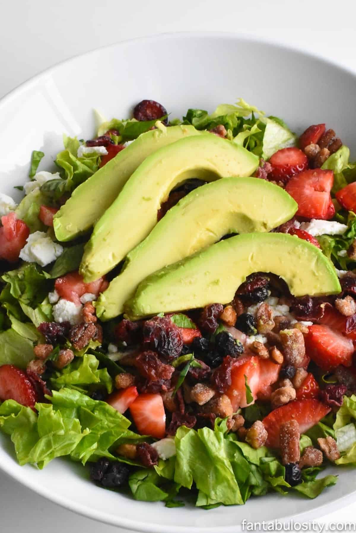 Summer side salad in white bowl, with avocado slices on top.