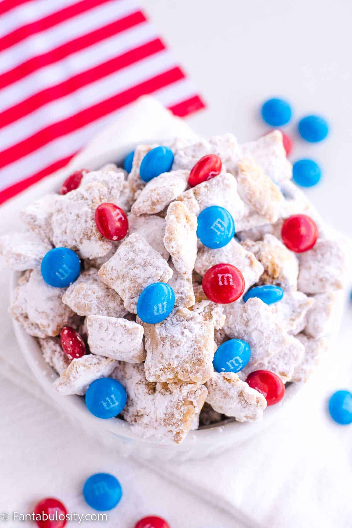 Fourth of July Muddy Buddies in white bowl, next to small American flag. 