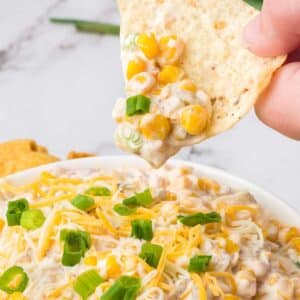 Chip holding a bite of crack corn dip, above bowl of dip.