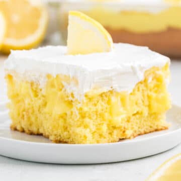 Slice of lemon poke cake on white plate, with lemon wedge on top.